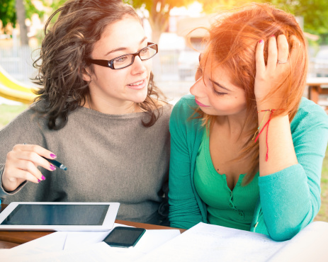 Two young women talking while studying using a tablet