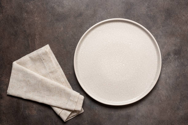 istock Empty beige plate with beige linen napkin on a dark brown background. Top view, flat lay. 1706340934