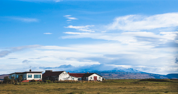 Village with farms in a rural area of the mountains of Iceland, with snowy mountains in the background.
