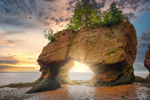 Colourful sunrise sky at low tide, with sun rays through Lover's Arch, Bay of Fundy, Hopewell Rocks Provincial Park, Hopewell Cape, New Brunswick, Canada.