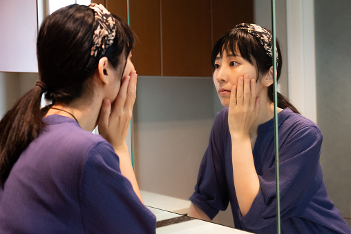 A woman at the washroom, concerned about the beauty of her skin.
She puts her hand on her cheek and thinks about the condition of her skin and aging.
Japanese female model.