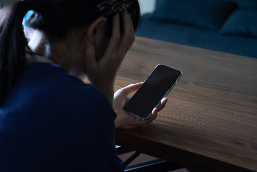 A woman who is frightened by a call coming from her phone.
She is holding her phone in a dark room.
A stalker on a social networking site.
Japanese female model.