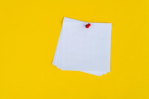 Blank adhesive sticky note and red thumbtack on yellow background