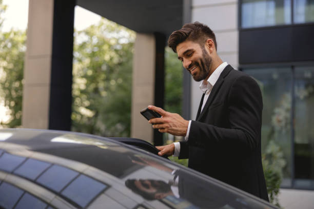 istock Cheerful businessman standing near car with mobile phone before sit inside 1706429053