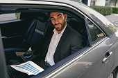Confidence businessman sitting on car backseat and working with documents and use laptop