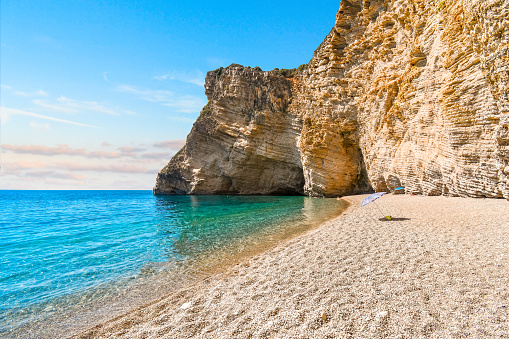 The cliffs and sandy shoreline of Paradise Beach, also known as Chomi Beach in the Aegean Sea off Corfu, Greece. Chomi, also known as Paradise beach, lies on the northwest coast of Corfu. It is close to Liapades and next to Iliodoros beach but you can access it only by sea.