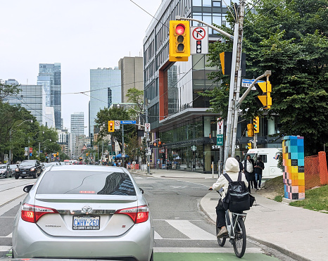 Toronto, Canada - August 24, 2023: Drivers, cyclists and pedestrians wait at the stoplight on College Street at Beverley Street. Summer afternoon in Toronto's Discovery District by the University of Toronto campus.