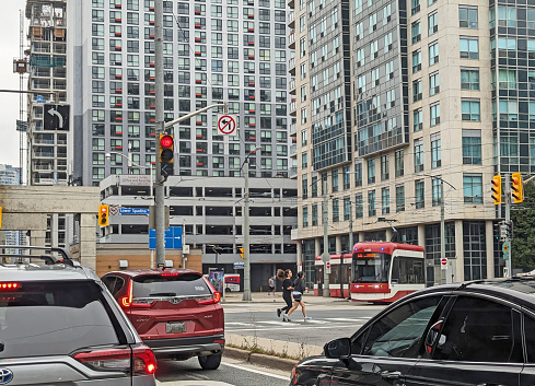 Toronto, Canada - August 24, 2023: Joggers head south on Lower Spadina Avenue in the Harbourfront neighbourhood. Background shows the TTC streetcars at the Queens Quay Loop. Summer afternoon with overcast skies downtown.