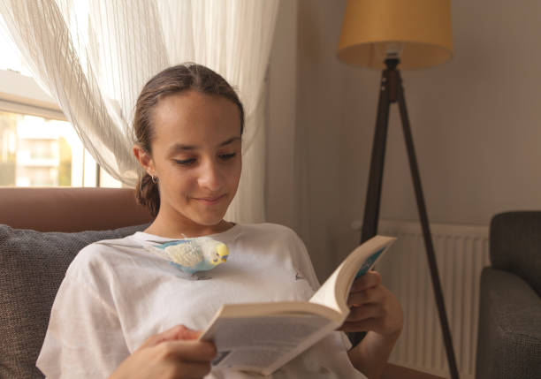 istock The young student reading a novel while a cute parakeet on her chest 1706437302