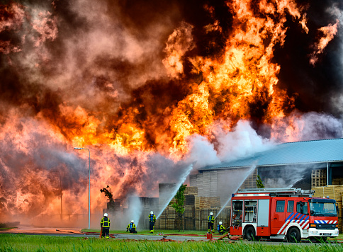 Fire fighters behind a fire engine trying to put out a fire in a factory and warehouse.