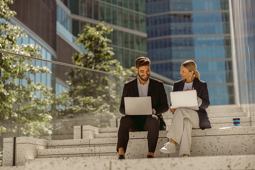 Business colleagues working on project while sitting outdoors on skyscrapers background