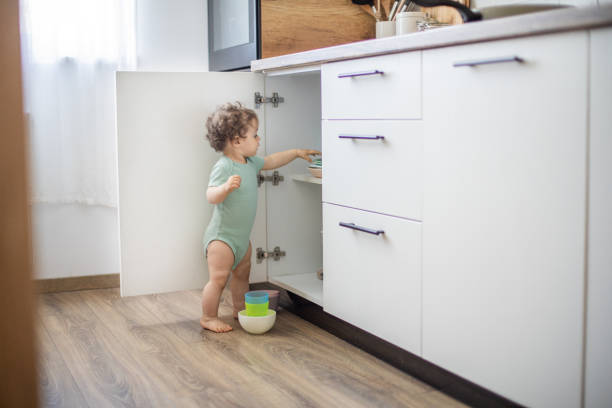 mignon curieux bébé caucasien ouvrir la porte du placard dans la cuisine et explorer le contenu - drawer domestic kitchen accessibility open photos et images de collection