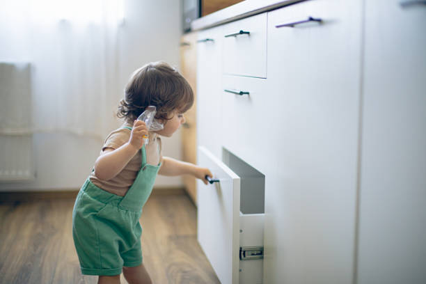 mignon curieux bébé caucasien ouvrir la porte du placard dans la cuisine et explorer le contenu - drawer domestic kitchen accessibility open photos et images de collection