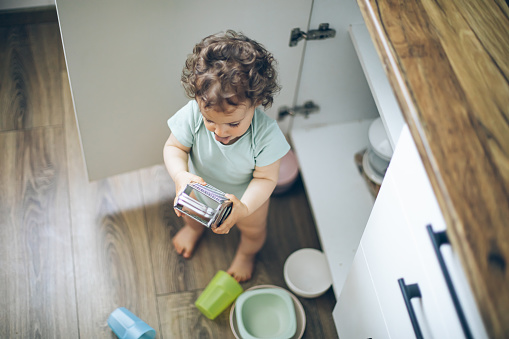 Cute baby playing with kitchen utensils in domestic kitchen