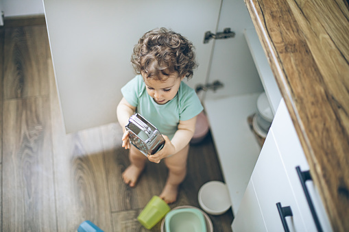 Cute baby playing with kitchen utensils in domestic kitchen