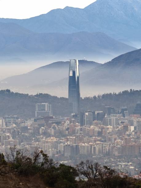 A landscape view, from nearby Andean foothills, of a smoggy Santiago in the middle of the austral winter, as pollution builds up in the mountain bowl accommodating the capital city due to the winter temperature inversion. Centre is the La Gran Torre Costanera, currently the tallest building in South America at a height of 300 metres.