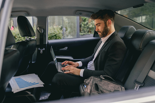 Businessman working on laptop sitting car backseat on the way to office. High quality photo