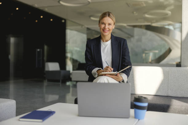 istock Pretty businesswoman making notes in note pad sitting on modern office background 1706478165