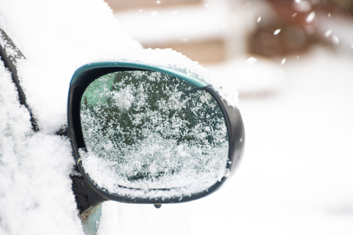 Rear view mirror of a car covered in snow on a winter day