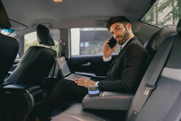 istock Handsome businessman in suit using personal computer and making phone call in taxi 1706500749