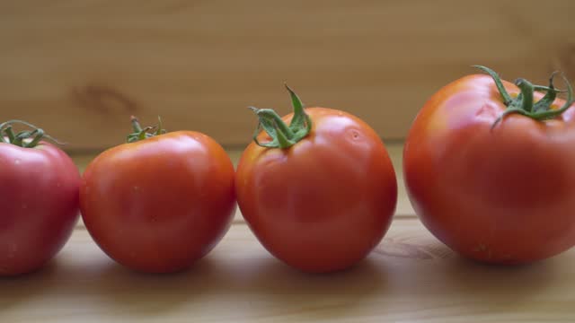 A row of red tomatoes of different sizes and shapes on a wooden table.