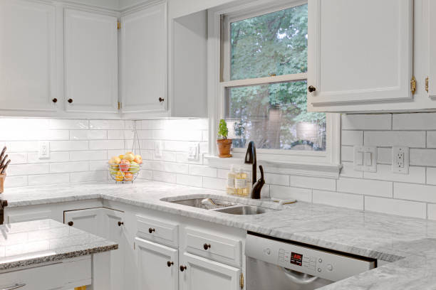 istock Clean Modern White Kitchen Interior with Stone Countertops and Granite Rolling Island. Fruit Basket in Corner with Empty Counters 1706515089