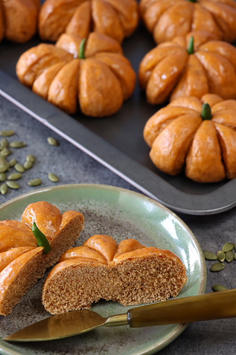 Stock photo showing close-up, elevated view of freshly baked, homemade, Halloween pumpkin designed rolls with green chilli pepper stalks on a baking sheet.