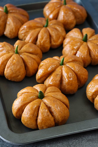 Stock photo showing close-up, elevated view of freshly baked, homemade, Halloween pumpkin designed rolls with green chilli pepper stalks on a baking sheet.