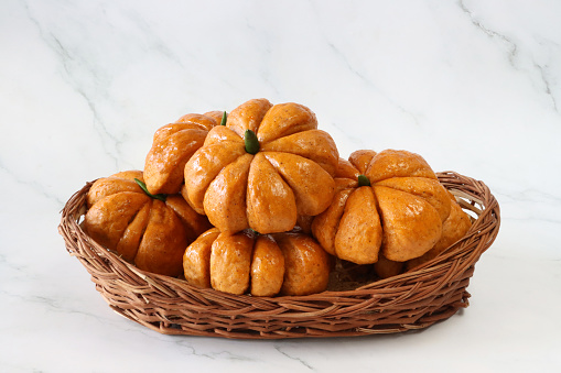 Stock photo showing close-up view of a wicker basket piled with freshly baked, homemade bread pumpkin designed rolls, ready to eat at a Halloween party. Green chilli peppers have been used as stalks and apricot jam has been used to glaze the buns.