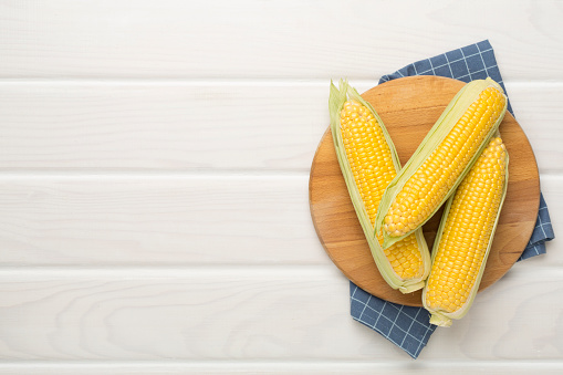 Fresh corn on cobs on wooden background, top view