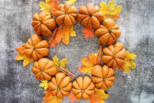 istock Image of pumpkin designed rolls with green chilli pepper stalks forming Halloween wreath, cinnamon sticks, autumnal leaves, homemade Halloween bread buns glazed with apricot jam, mottled grey background, copy space, elevated view 1706599859
