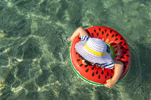 High angle view of young girl wearing sun hat and sunglasses in inflatable swimming ring in the sea. Summer vacation fashion concept.