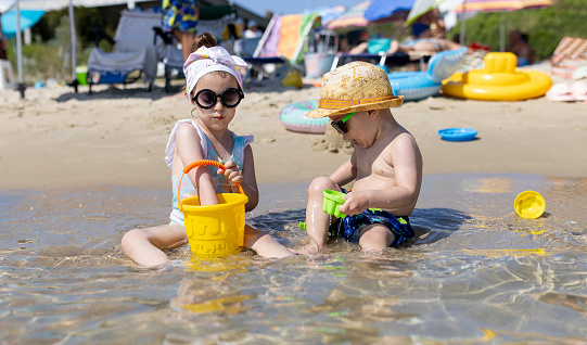Kids playing on the beach. Boy and girl with plastic toy buckets and spade at the sea shore. Childhood and summer vacation concept.