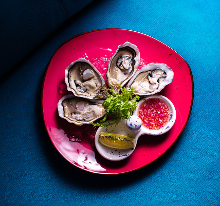 Fresh oysters in a red plate with ice and lemon on a blue background