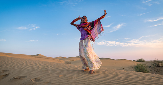 Young Indian girl dancing on a sand dune, Thar Desert, Rajasthan, India