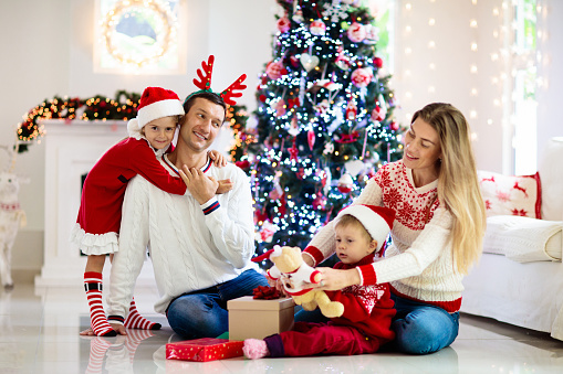 Family celebrating Christmas. Parents and kids decorate Xmas tree and open gifts. Child with present box. Kid opening presents.  Home decoration for winter holidays. Festive decorated living room.