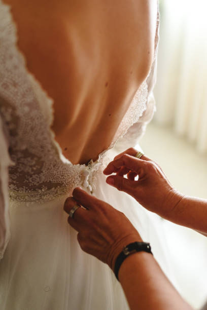istock Seamstress buttoning the pretty wedding dress, elegant and bare back. 1706697374