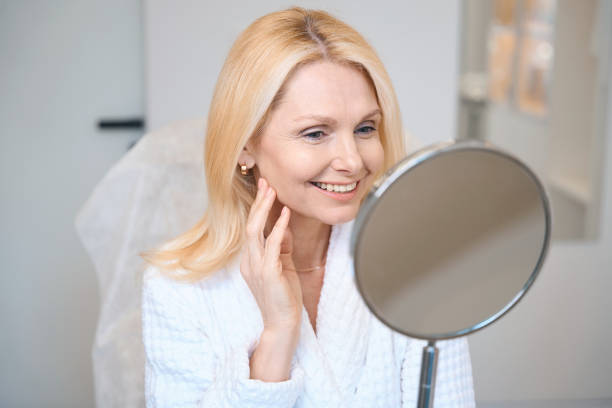 istock Smiling mature lady looking in mirror at cosmetologist office 1706715286