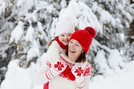 Mother and child in knitted winter hats play in snow on family Christmas vacation. Handmade wool hat and scarf for mom and kid. Knitting for kids. Knit outerwear. Woman and little girl in snowy park.
