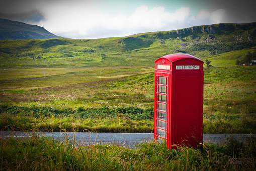Typical red English telephone box in a rural area near a road.