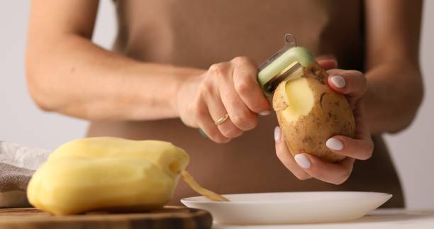 молодая женщина чистит картошку. процесс приготовления пищи. - potato skin стоковые фото и изображения