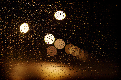 View through the wet window at night with water drops and blurry city lights.