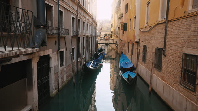 SLO MO Tilt Down shot of Boats Moored in Calm Narrow Canal amidst Old Buildings in Venice