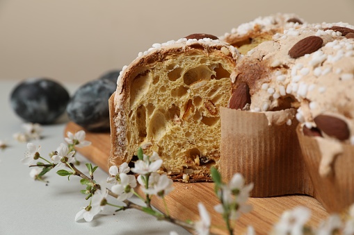 Pieces of delicious Italian Easter dove cake (traditional Colomba di Pasqua), branch with flowers and painted eggs on light grey table, closeup