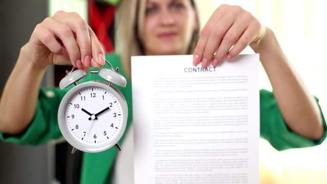 The woman holds out an alarm clock and a contract