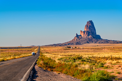 A highway in northeastern Arizona near Four Corners leading to the famed Monument Valley with a large rock formation along the right side.