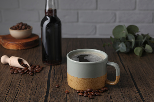 Mug of aromatic coffee, syrup and beans on wooden table