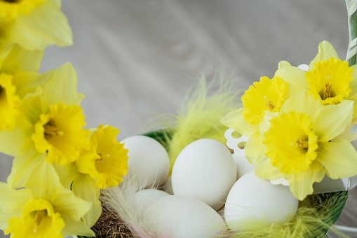 Easter light blue eggs in white vintage metal holder with feathers, ribbon, yellow chrysanthemums flowers and blank paper for text on yellow background. Mock up. Spring Happy Easter holiday card.