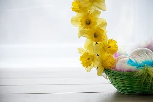 Copypace of decorative homemade basket to place eggs. Colorful feathers and yellow daffodils are used.