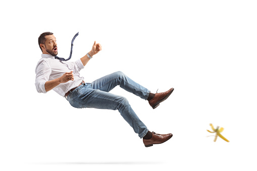 Full length profile shot of a young man falling on a banana skin isolated on white background